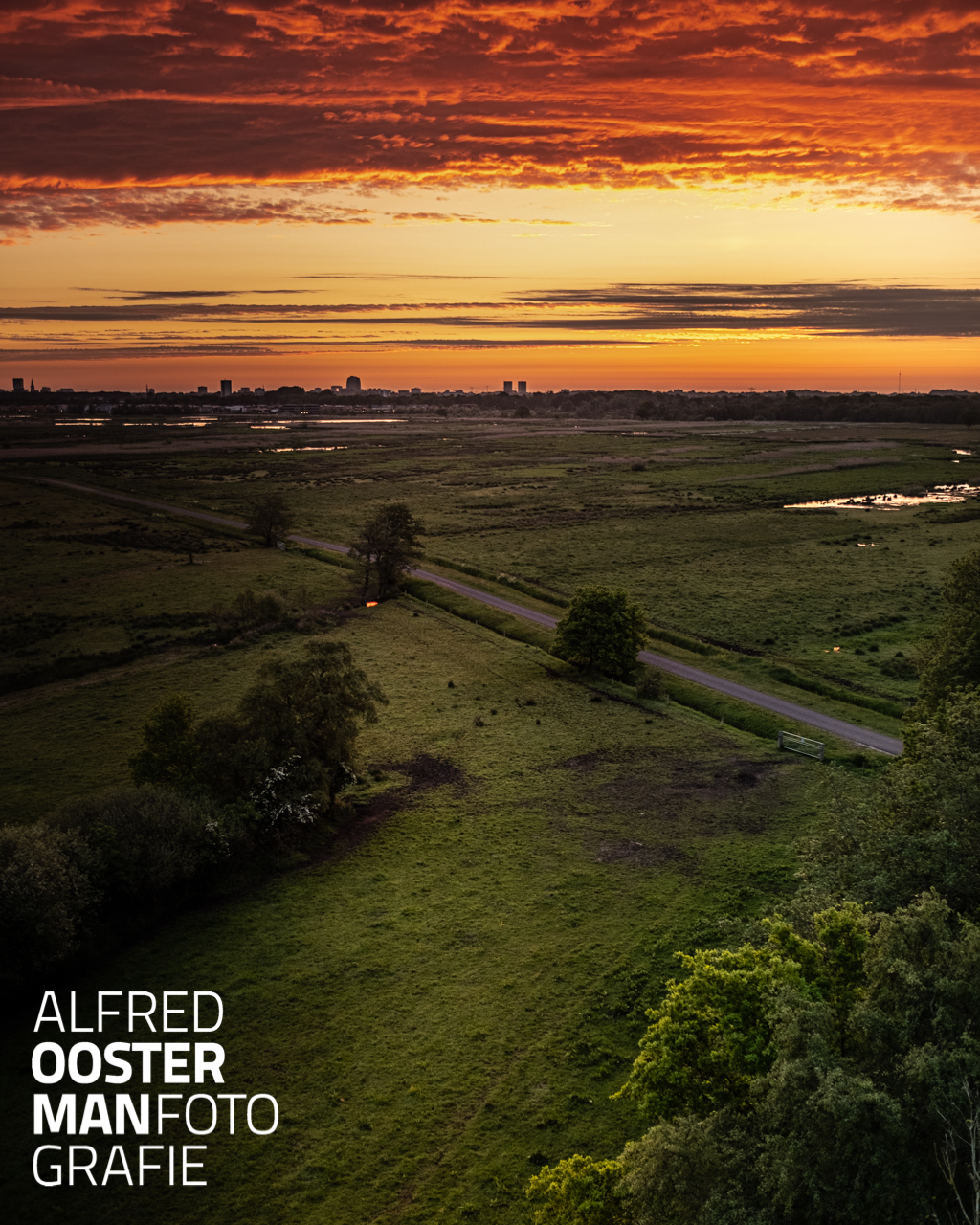 Standpunt In de serie die ik in 'de Onlanden' maak fotografeer ik vaak vanaf ooghoogte. Daarbij gebruik ik een perspectief wat de serie extra ondersteunt. Een constante die helpt om 'in het beeld te stappen'. Natuurlijk gaat dat niet altijd op en kies ik er ook voor om dat anders te doen als dat voor het onderwerp beter is. Mijn keuze bij deze foto was om echt hoger te gaan. De uitkijktoren in 'het Beeld' in 'de Onlanden' steekt ruim boven de bomen uit en geeft een mooi overzicht waarbij de structuur van dit gebied goed zichtbaar is. En vanmorgen had ik geluk, een heftig gekleurde lucht kondigde de zon aan. 5.14 uur stipt, de zon laat het eerste streepje boven de horizon zien terwijl ik op de fiets richting mijn ontbijt ga.